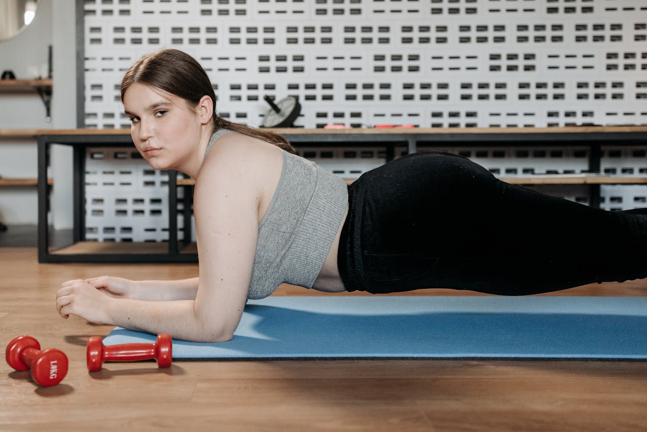 Woman doing planks on a yoga mat indoors with dumbbells showing dedication to fitness.
