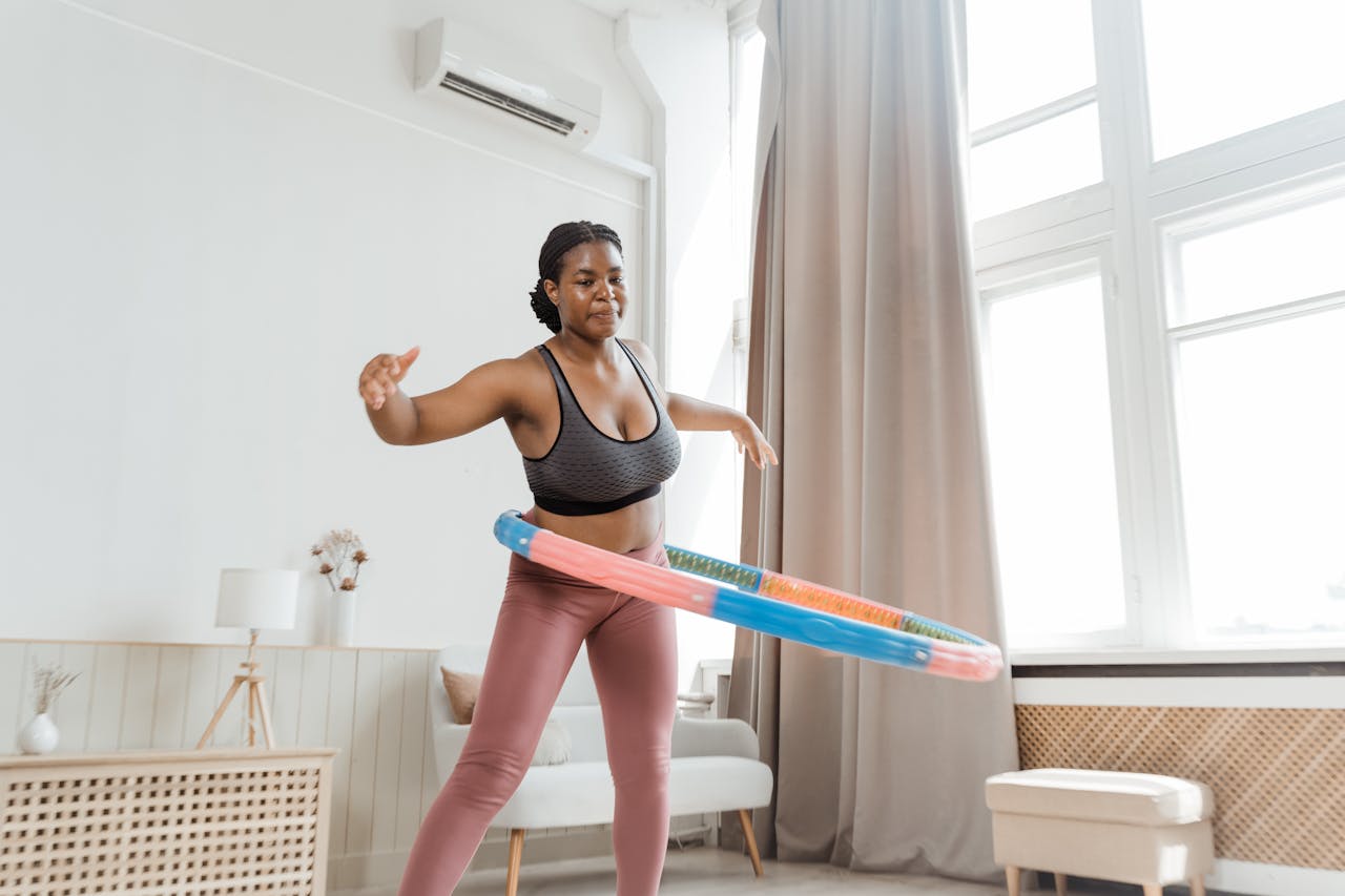 Black woman hula hooping at home, showcasing indoor fitness and health.